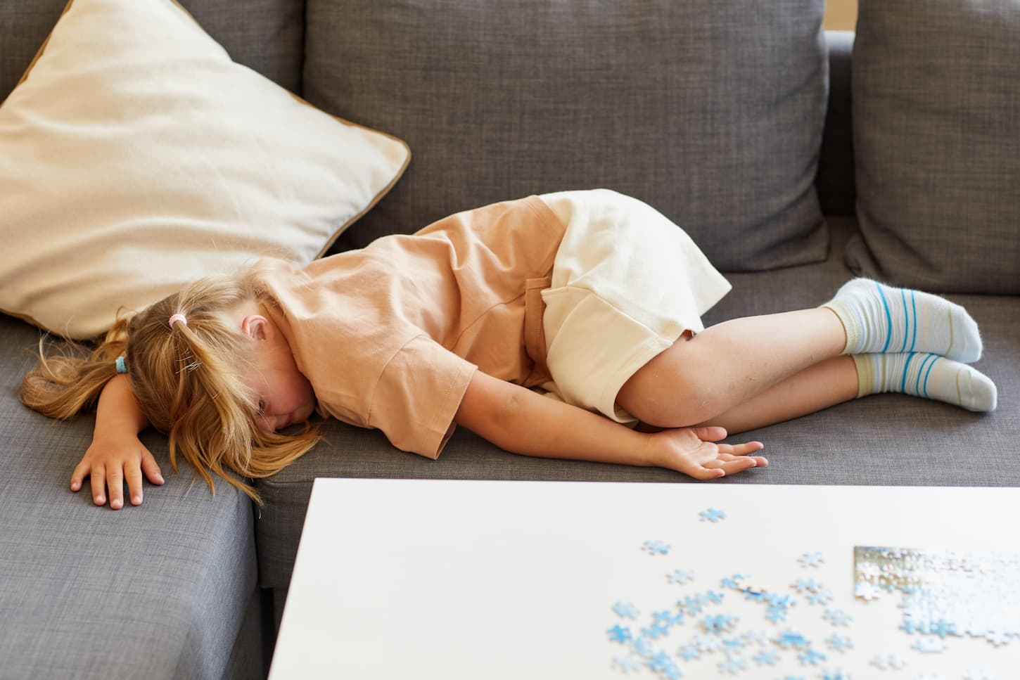 An image of a cute girl with down syndrome falling asleep on the sofa while playing board games at home.