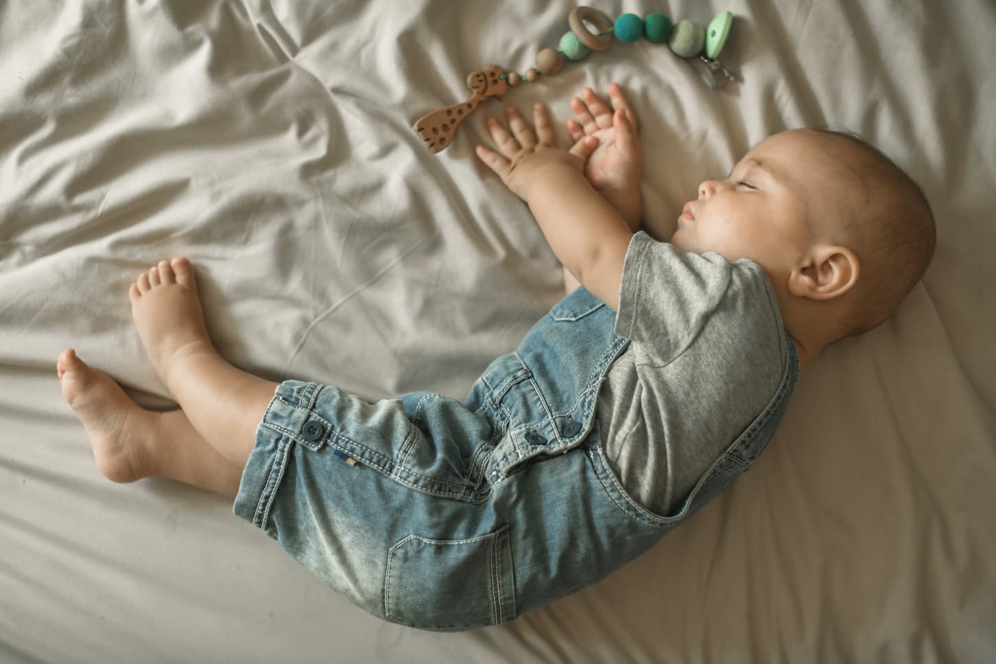 An image of a 7-month-old baby sleeping with a juniper toy on the bed.