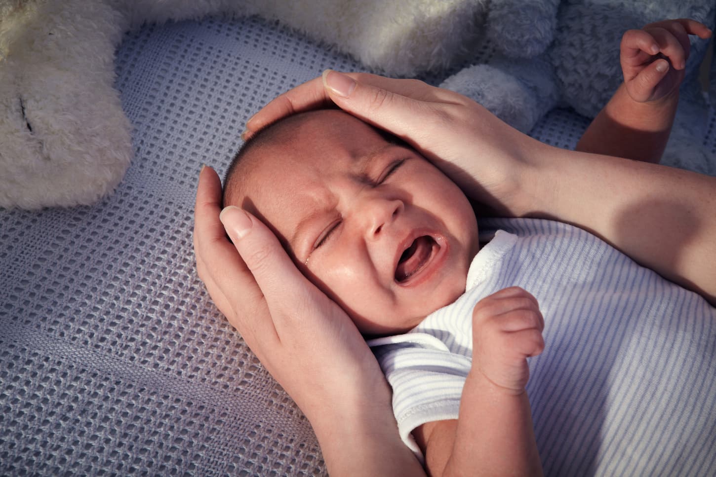 An image of a baby boy crying in a crib before going to bed.
