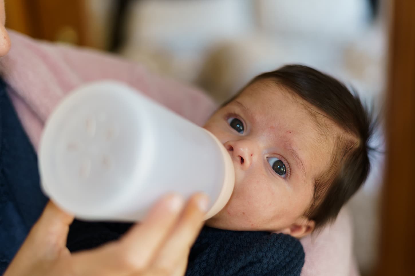An image of a newborn baby feeding on a bottle of milk while looking at the camera.