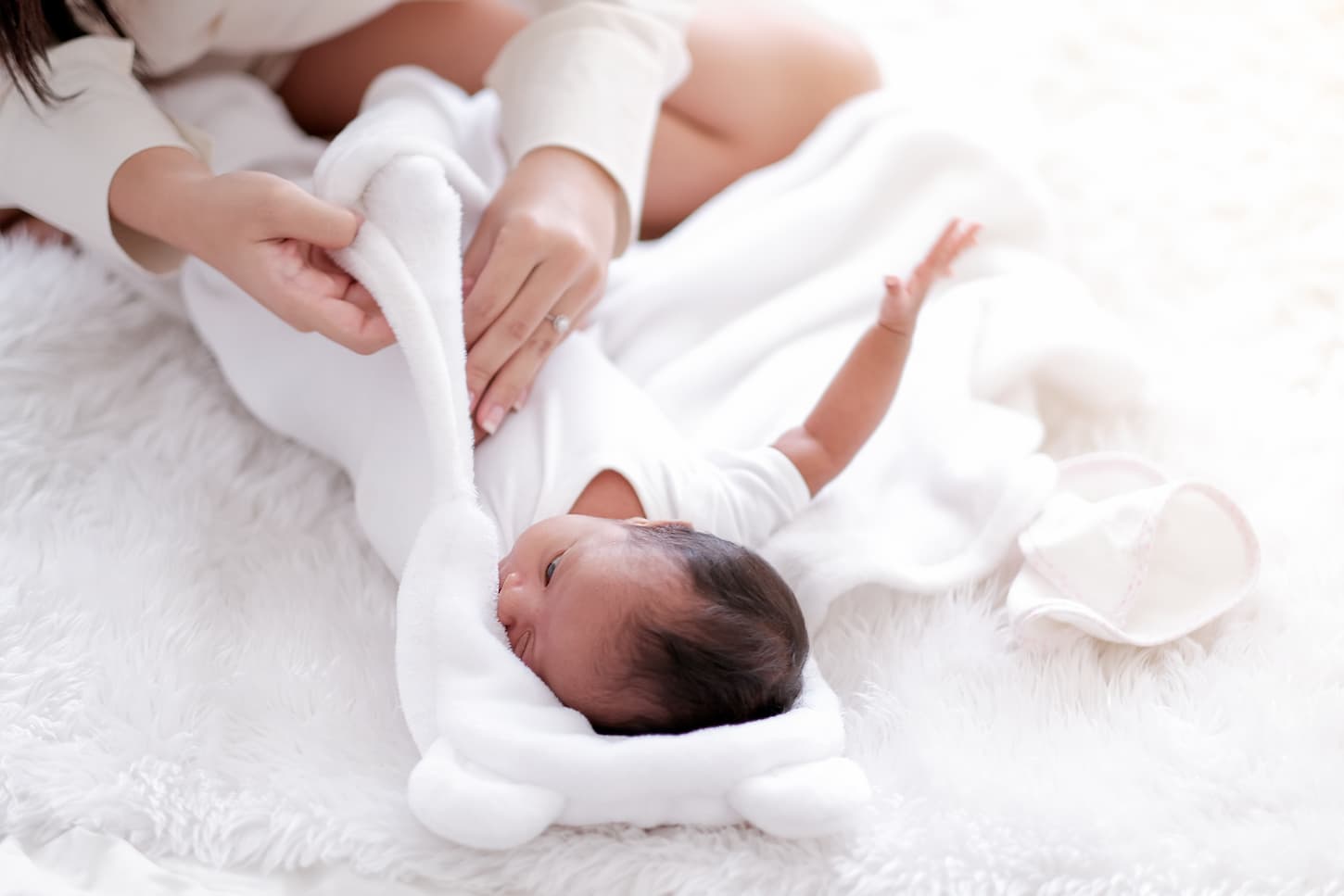 An image of a mother while swaddling her newborn baby with white cloth.