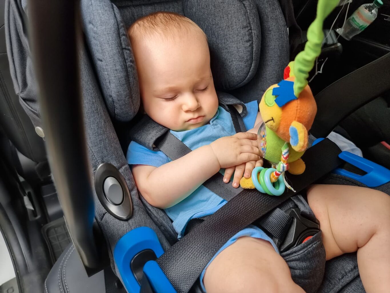 An image of a cute little baby boy sleeping in a car in the safety seat