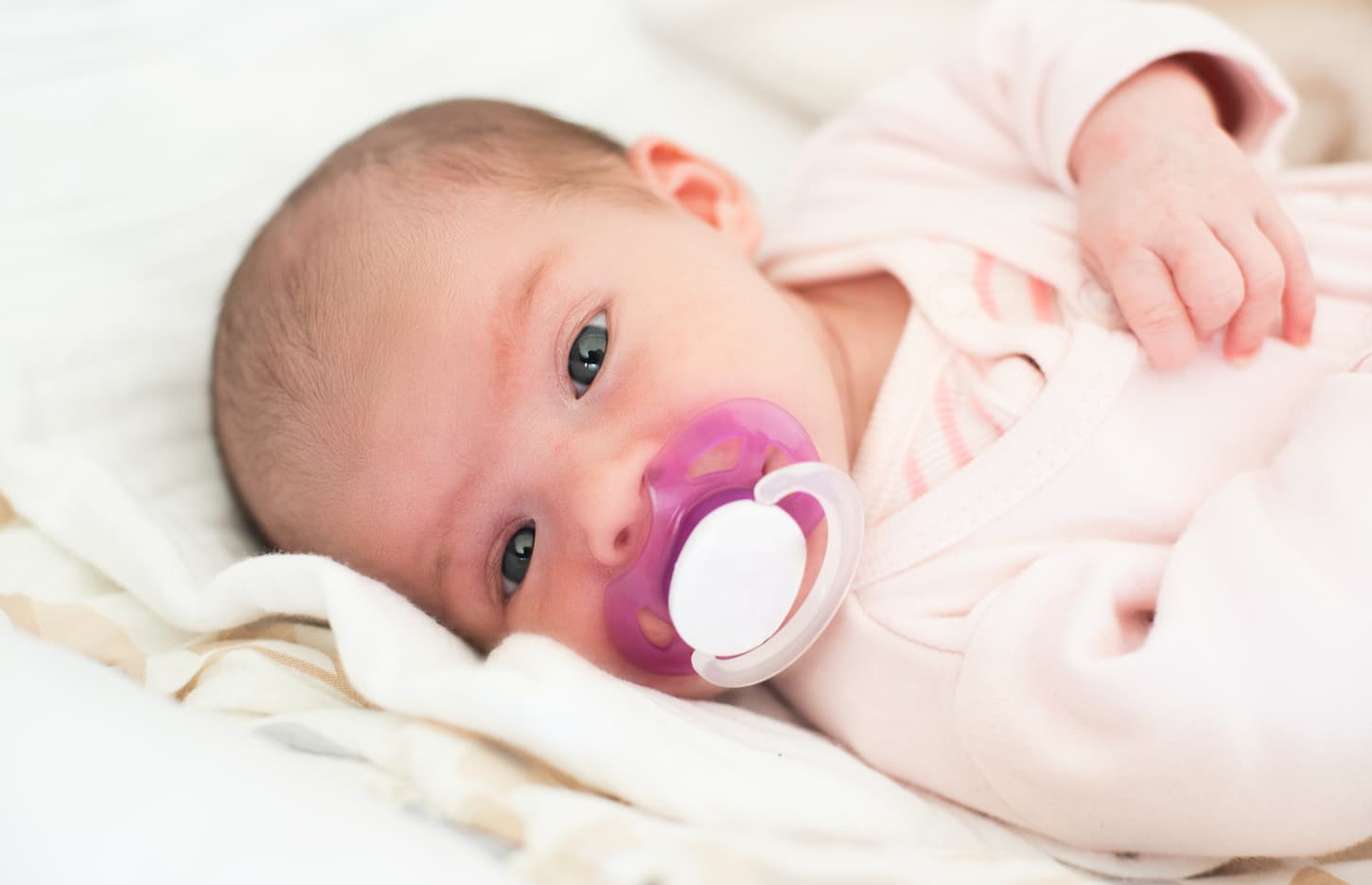 An image of a newborn baby lying on its side with a white soothing pacifier.