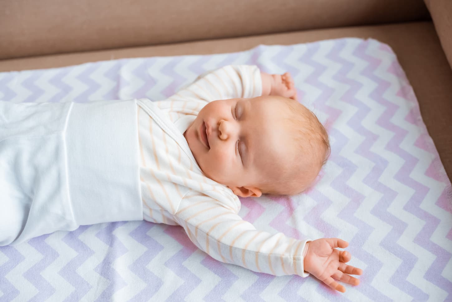 An image of an adorable newborn baby with closed eyes and raised hands during a nap.