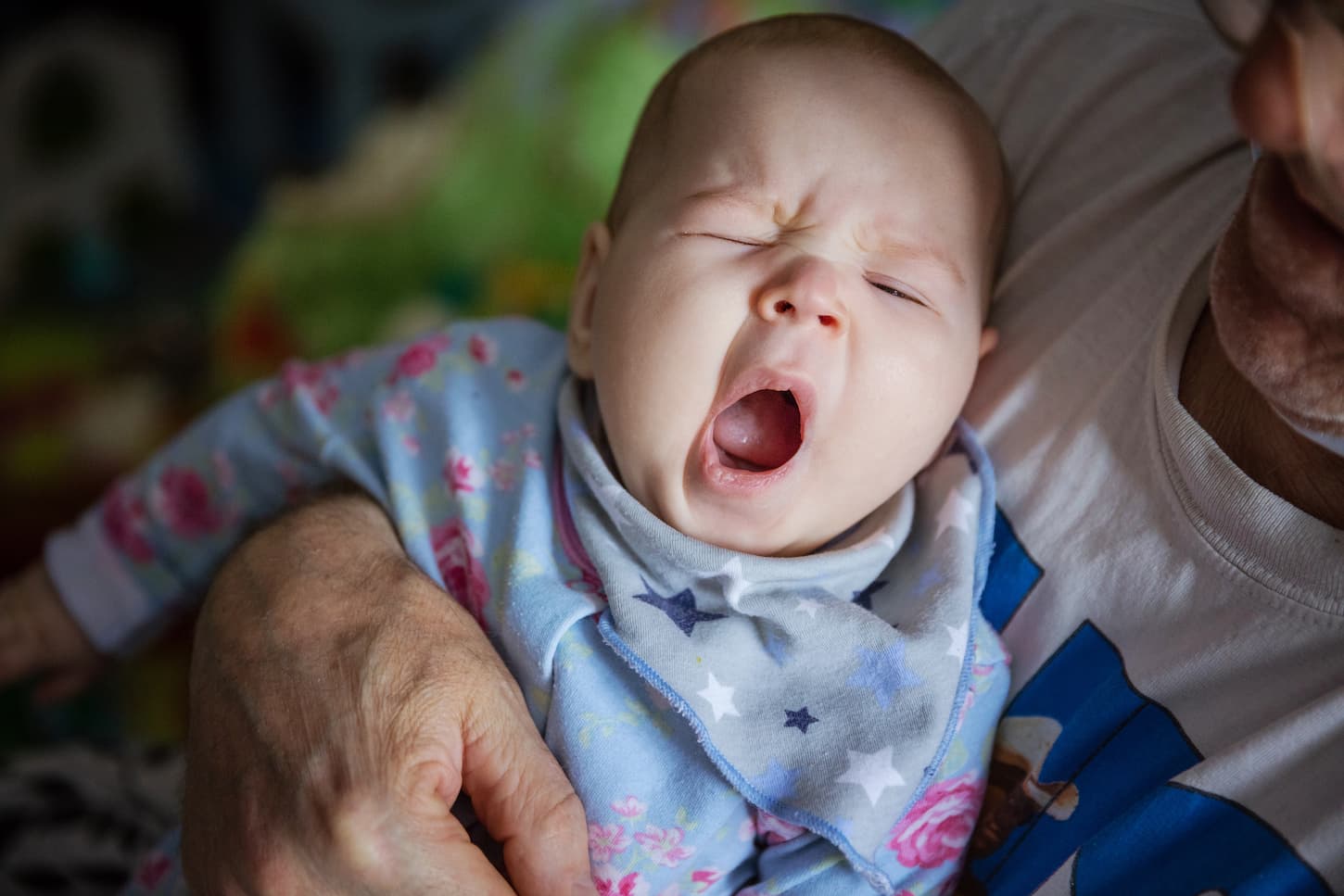 An image of a grandfather rocking the baby who's yawning to sleep.