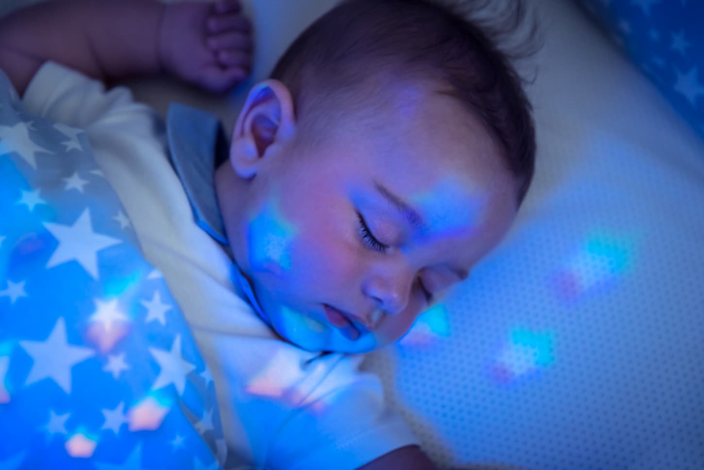 An image of a baby boy sleeping in his bed with star-shaped night lights in the whole room.