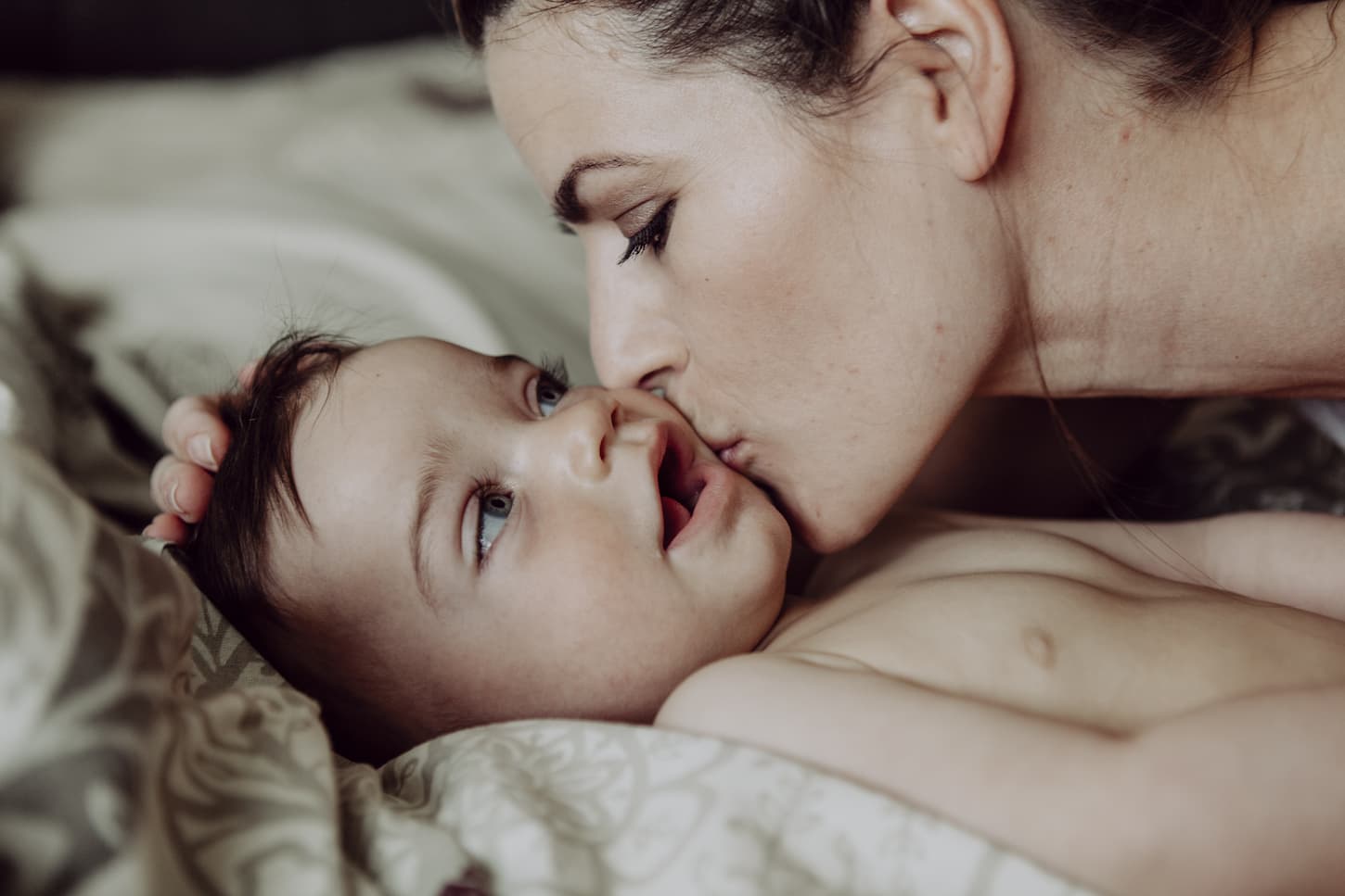 An image of a mother cuddling her baby son on the bed.