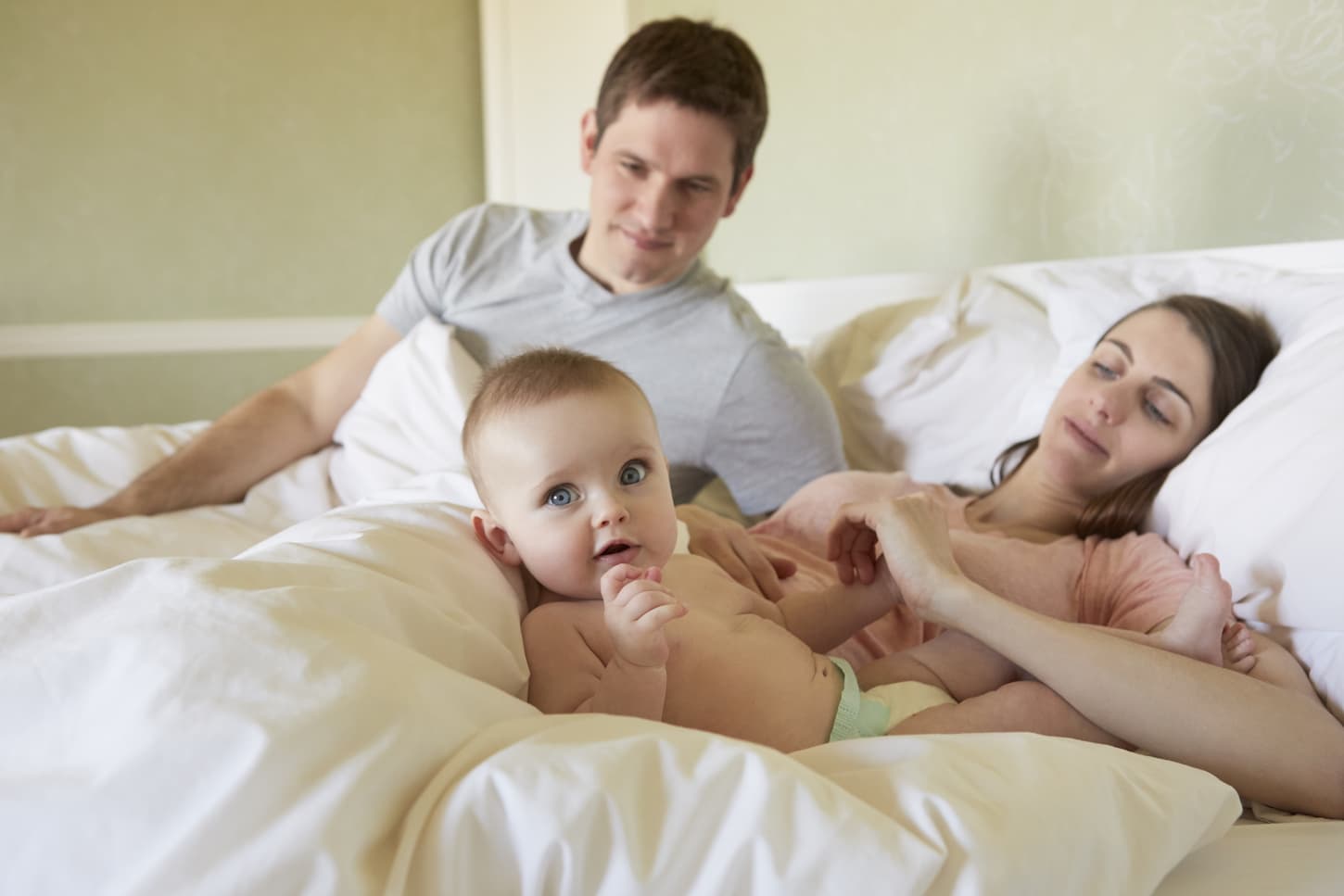 An image of a baby girl lying in bed with her parents.