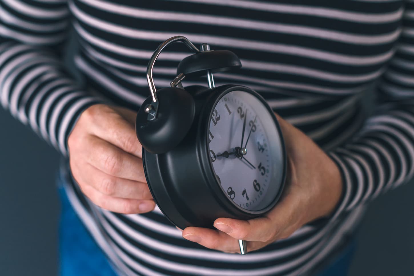 An image of a Woman winding a retro alarm clock, the concept of daylight saving time, selective focus.