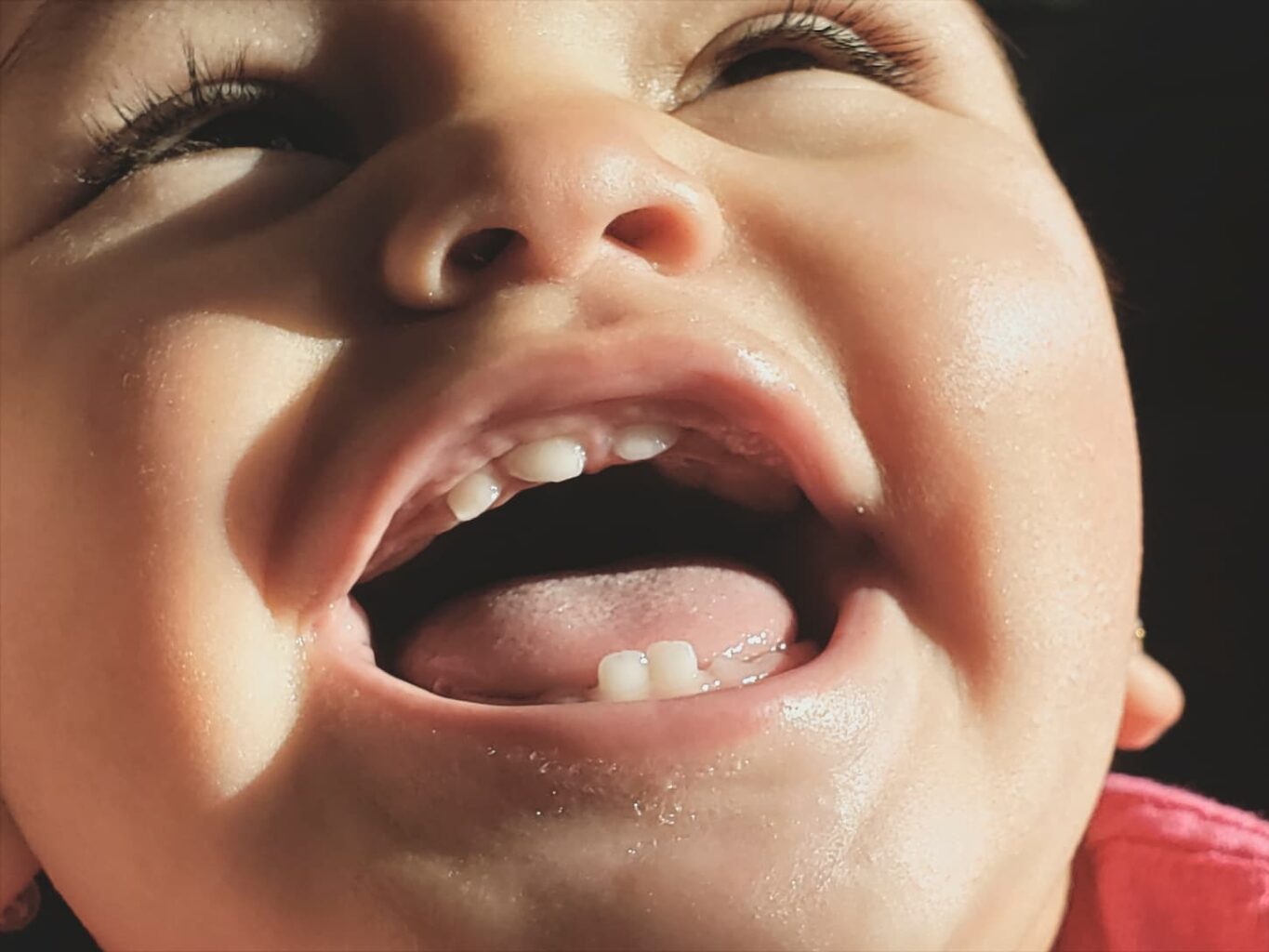 An image of a baby girl laughing hysterically showing her newly acquired teeth in the process.