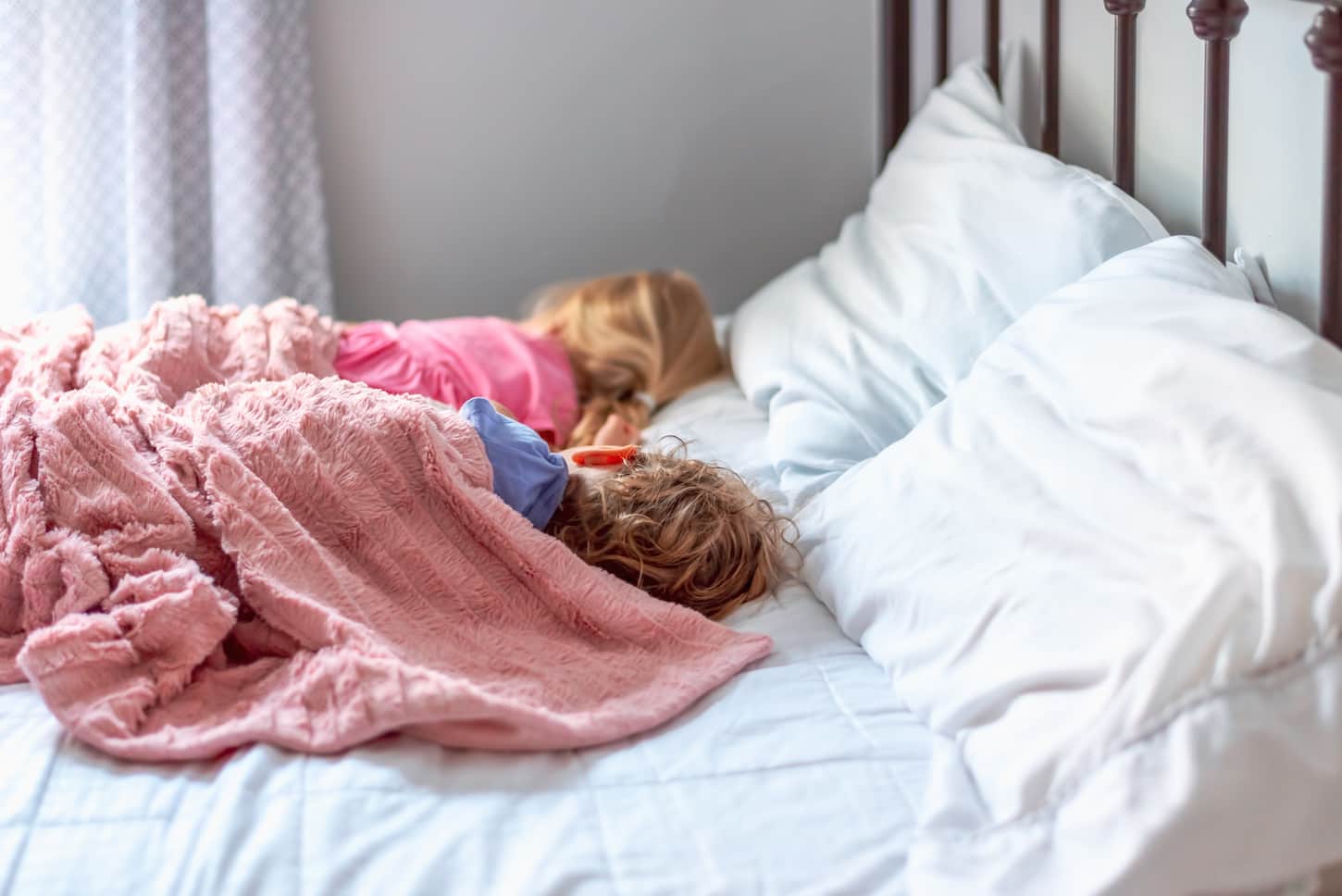 An image of two little girls taking a nap on a big white bed.